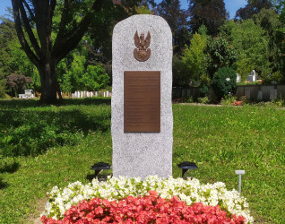 Granitowy obelisk z tablicą upamiętniającą żołnierzy 2. Dywizji Strzelców, otoczony kwiatami i zielenią na cmentarzu.