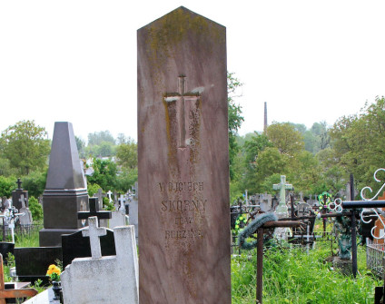 Fotografia cmentarna przedstawia wysoki kamienny obelisk na stopniowanym cokole z rytym krzyżem i napisem Wojciech Skorny oraz rodzina