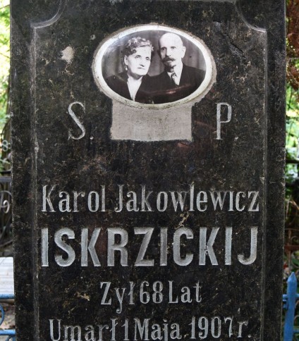 Nagrobek Karola Jakowlewicza Iskrzickijego z owalnym ceramicznym medalionem przedstawiającym mężczyznę z wąsem w garniturze i kobietę z kręconymi włosami w garsonce, noszącą biżuterię z pereł. Napis: 'Karol Jakowlewicz Iskrzickij, żył 68 lat, umarł 1 maja 1907'.