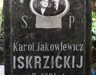 Nagrobek Karola Jakowlewicza Iskrzickijego z owalnym ceramicznym medalionem przedstawiającym mężczyznę z wąsem w garniturze i kobietę z kręconymi włosami w garsonce, noszącą biżuterię z pereł. Napis: 'Karol Jakowlewicz Iskrzickij, żył 68 lat, umarł 1 maja 1907'.
