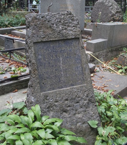 Grób Feliksa Iphorskiego Lenkiewicza oznaczony krzyżem na cokole w formie głazu z płyciną z inskrypcją z przodu. Widoczna otaczająca zieleń i inne groby.