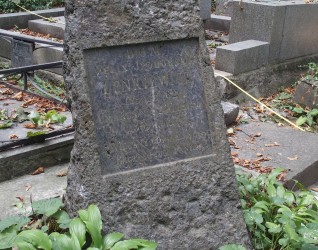 Grób Feliksa Iphorskiego Lenkiewicza oznaczony krzyżem na cokole w formie głazu z płyciną z inskrypcją z przodu. Widoczna otaczająca zieleń i inne groby.