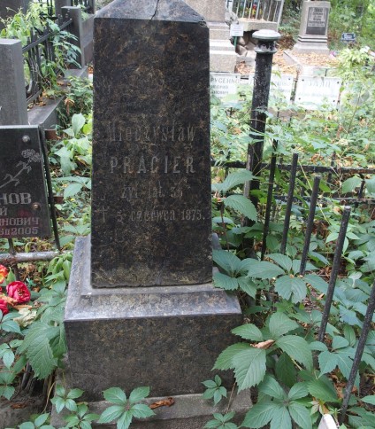 Nagrobek Mieczysława Pragiera z wyrytą inskrypcją, otoczony zielenią i metalowym ogrodzeniem. W pobliżu inne nagrobki we wspólnej kwaterze.