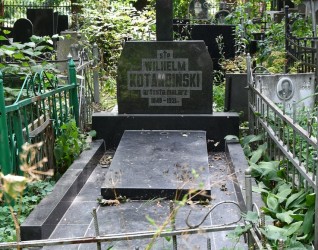 Grób Wilhelma Kotarbińskiego z prostokątną płytą nagrobną otoczoną dwoma blokami. Z płyty wznosi się krzyż z inskrypcją w reliefie. Otoczony zielenią i metalowym ogrodzeniem.