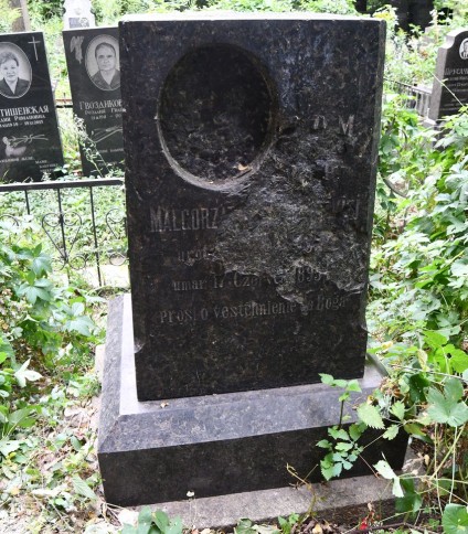 Nagrobek Małgorzaty z dwustopniowym cokołem i podstawą. Z przodu inskrypcja i owalne wgłębienie na brakujący medalion. Otoczony zielenią i innymi nagrobkami.