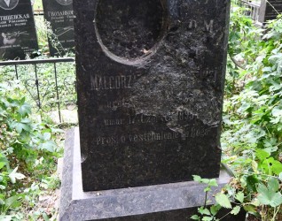 Nagrobek Małgorzaty z dwustopniowym cokołem i podstawą. Z przodu inskrypcja i owalne wgłębienie na brakujący medalion. Otoczony zielenią i innymi nagrobkami.