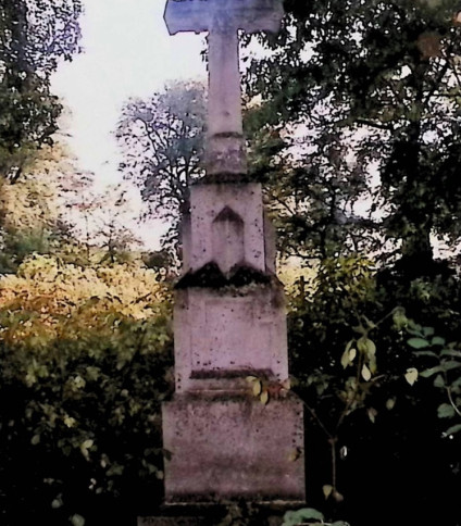 Nagrobek Magdaleny i Franciszka Białkowskich z krzyżem na trójstopniowym cokole otoczony drzewami.