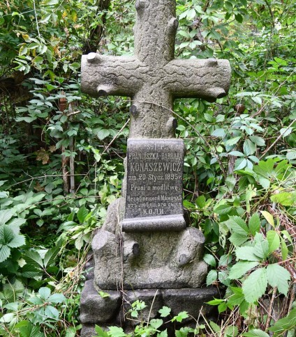 Nagrobek Franciszki Konaszewicz z krzyżem przypominającym pień drzewa. Z przodu tablica w reliefie w formie zwoju z inskrypcją. Cokół stylizowany na stos kamieni, otoczony zielenią.