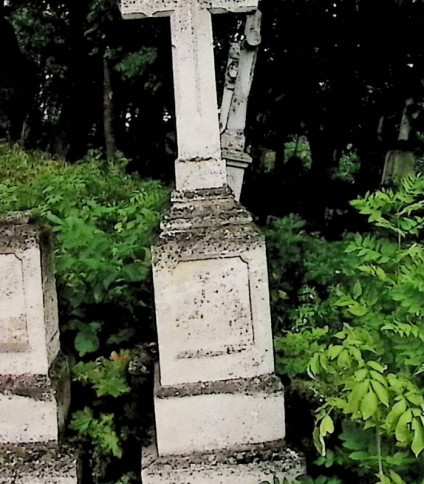 Nagrobek z krzyżem na trójstopniowym cokole otoczony zielenią. Krzyż ma spłaszczone ostrosłupy na końcach i żłobienia na licu. Cokół ma ścięte i profilowane krawędzie z płyciną inskrypcyjną.