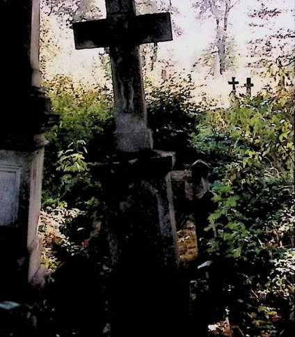 Nagrobek Teodora Skrockiego z krzyżem na dwustopniowym cokole, z reliefem Chrystusa na przecięciu ramion. Otoczony roślinnością.