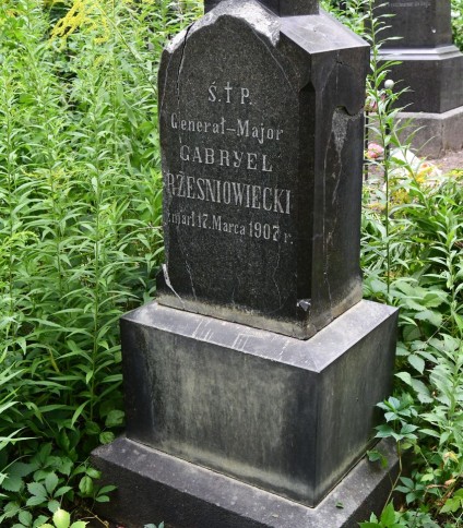 Nagrobek Generała-Majora Gabriela Rześniowieckiego z wyrytą inskrypcją, otoczony zielenią. Kamień ma stopniowaną podstawę i spadzisty wierzchołek.