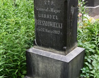 Nagrobek Generała-Majora Gabriela Rześniowieckiego z wyrytą inskrypcją, otoczony zielenią. Kamień ma stopniowaną podstawę i spadzisty wierzchołek.