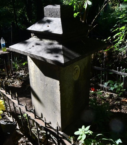 Nagrobek Stanisława Koscieszy Rakowskiego z krzyżem na cokole, z ściętymi krawędziami i inskrypcją. Powyżej wgłębienie na medalion z fotografią, otoczone zielenią.