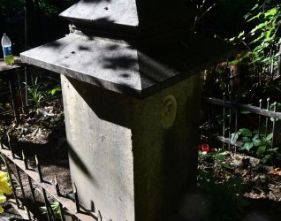 Nagrobek Stanisława Koscieszy Rakowskiego z krzyżem na cokole, z ściętymi krawędziami i inskrypcją. Powyżej wgłębienie na medalion z fotografią, otoczone zielenią.