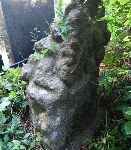 Nagrobek z cokołem stylizowanym na stos kamieni, z reliefową tablicą z inskrypcją i krzyżem z rozszerzającym się dolnym ramieniem i półkolistymi zakończeniami.