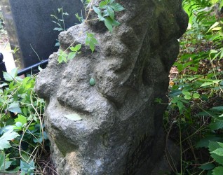 Nagrobek z cokołem stylizowanym na stos kamieni, z reliefową tablicą z inskrypcją i krzyżem z rozszerzającym się dolnym ramieniem i półkolistymi zakończeniami.