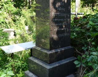 Nagrobek Baltazara Krzyżanowskiego z inskrypcją na trzystopniowym cokole otoczony zielenią.