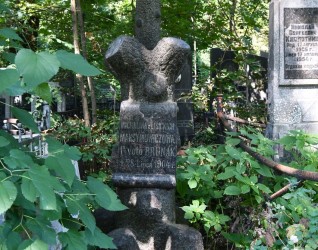 Grób oznaczony krzyżem na cokole, oba stylizowane na pnie drzew. Z przodu tablica z inskrypcją w reliefie w formie rozwiniętego zwoju. Otoczony zielenią.