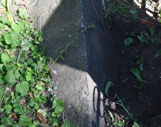 Kamienny cokół o ściętych górnych krawędziach, otoczony trawą i roślinami. Na przedniej płycinie naroża ścięte ćwierćkoliście z wyrytą inskrypcją.