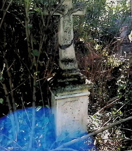 Nagrobek Justyny i Wasyla Bukaczuków z krzyżem na cokole otoczonym roślinnością. Krzyż ma relief Chrystusa na przecięciu ramion i inskrypcję poniżej.