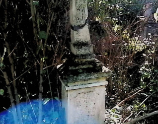 Nagrobek Justyny i Wasyla Bukaczuków z krzyżem na cokole otoczonym roślinnością. Krzyż ma relief Chrystusa na przecięciu ramion i inskrypcję poniżej.