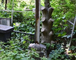 Grób Marii i Mieczysława Korzeniowskich z krzyżem stalowym na cokole przypominającym stos kamieni. Krzyż bez poprzecznej belki. Otoczony gęstą zielenią.