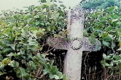 Nagrobek z krzyżem na niskim cokole, otoczony zielenią. Krzyż ma półkoliste zakończenia z gwiazdkami w płaskorzeźbie i koronę cierniową na przecięciu ramion. Poniżej czaszka z piszczelami w płaskorzeźbie.