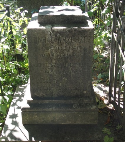 Nagrobek Konrada Wrzeszcza z inskrypcjami, pierwotnie oznaczony krzyżem. Dwustopniowy cokół o profilowanych i ściętych krawędziach, otoczony zielenią.