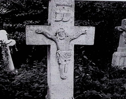 Nagrobek z krzyżem na cokole. Na przecięciu ramion relief Chrystusa, powyżej titulus. Cokół ma profilowane górne krawędzie i inskrypcję w ramie z przodu.