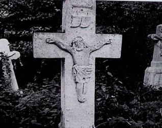 Nagrobek z krzyżem na cokole. Na przecięciu ramion relief Chrystusa, powyżej titulus. Cokół ma profilowane górne krawędzie i inskrypcję w ramie z przodu.