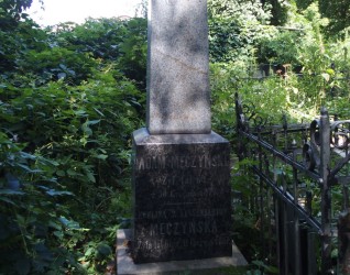 Nagrobek Eweliny i Adama Męczyńskich. Brak oryginalnego krzyża, widoczny żeliwny trzpień. Cokół dwustopniowy, pierwszy stopień o ściętych krawędziach, drugi zwężający się ku górze. Otoczony zielenią.