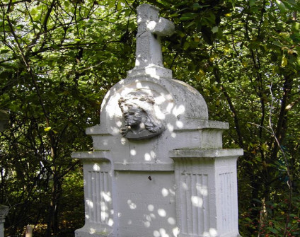 Nagrobek z krzyżem na cokole otoczony drzewami. Krzyż z medalionem 'INRI' i reliefem głowy Chrystusa w koronie cierniowej. Kanelurowane pilastry z kapitelami w jodełkę otaczają płytę z inskrypcją.