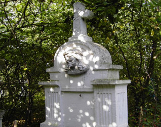 Nagrobek z krzyżem na cokole otoczony drzewami. Krzyż z medalionem 'INRI' i reliefem głowy Chrystusa w koronie cierniowej. Kanelurowane pilastry z kapitelami w jodełkę otaczają płytę z inskrypcją.