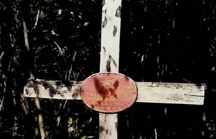 Drewniany krzyż oznaczający grób Jana i Józefa Kuriańskich. Na przecięciu ramion krzyża znajduje się owalna żeliwna tablica z malowaną inskrypcją.