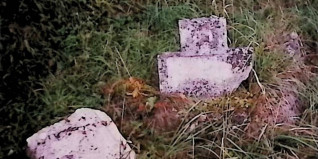 Przełamana kamienna stela na trawiastym terenie, pierwotnie oznaczona krzyżem. Krzyż jest nieobecny, a stela przełamana na pół. Na froncie cokołu widoczna inskrypcja.