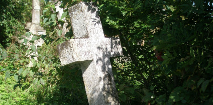 Nagrobek Mikołaja Maruszewskiego z krzyżem na niskim cokole. U podstawy czaszka z piszczelami, powyżej inskrypcja. Otoczony zielenią.