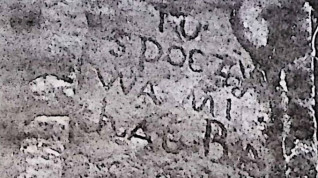 Zbliżenie na zwietrzały kamienny cokół z inskrypcją w prostokątnej płycinie o ćwierćkolistych narożach. Tekst jest częściowo czytelny.