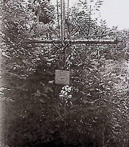 Żeliwny krzyż na betonowym cokole z motywami esownic i dwoma kołami z krzyżykiem. Na przecięciu figura Chrystusa; poniżej metalowa tabliczka z inskrypcją.