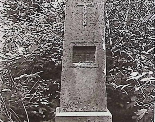 Nagrobek Tadeusza Kościńskiego z obeliskiem z płaskorzeźbionym krzyżem i metalową tablicą w prostokątnej niszy, otoczony żeliwnym ogrodzeniem z piaskowcowymi słupkami.