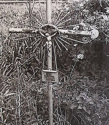 Żeliwny krzyż na cokole z esownicami i figurą Chrystusa w promienistej glorii na przecięciu ramion. Poniżej metalowa tabliczka z inskrypcją. Cokół zwęża się ku górze.