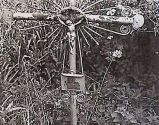 Żeliwny krzyż na cokole z esownicami i figurą Chrystusa w promienistej glorii na przecięciu ramion. Poniżej metalowa tabliczka z inskrypcją. Cokół zwęża się ku górze.