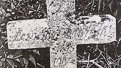 Prosty krzyż oznaczający grób Jana Dąbroskiego z wyrytą inskrypcją, otoczony trawą.