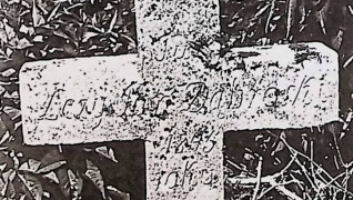 Prosty krzyż oznaczający grób Jana Dąbroskiego z wyrytą inskrypcją, otoczony trawą.