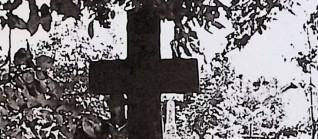 Grób z krzyżem na cokole, ozdobionym guzkami i rozetami. Na cokole wyryte serce z krzyżykiem i oszklona tablica z inskrypcją.