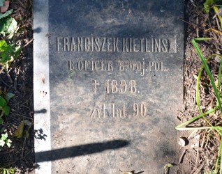Polerowany nagrobek Franciszka Kietlińskiego o ściętych krawędziach, z napisem i symbolem krzyża. Otoczony trawą i ziemią.