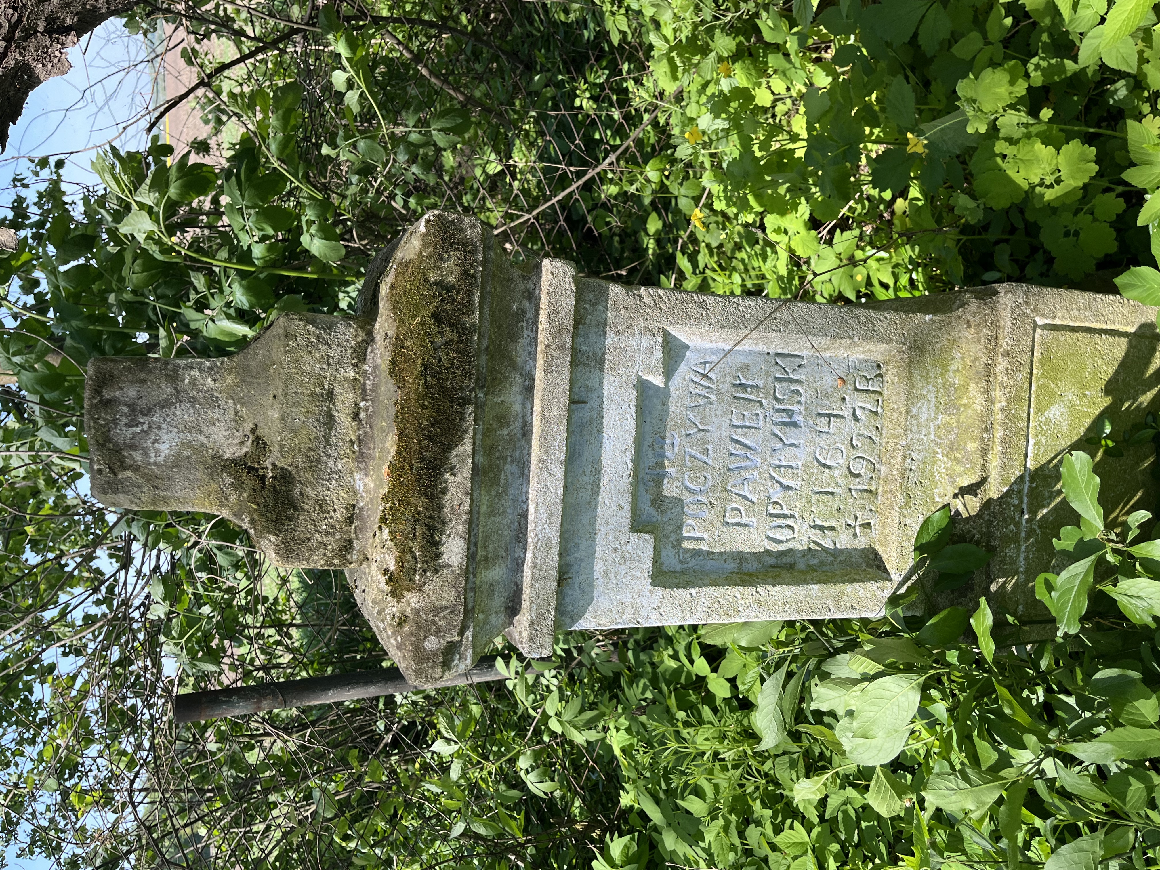 Old tombstone with inscription 'Here rests Paweł Kopytyński, lived 64 years, died 1922' surrounded by green foliage at the cemetery in Kościejów.