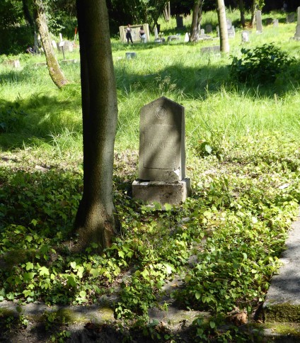 Nagrobek Marii Zwyrtek z dwuspadową stelą na cokole na trawiastym cmentarzu. Stela rozszerza się ku dołowi, u góry owalna płycina i prostokątna tablica inskrypcyjna.