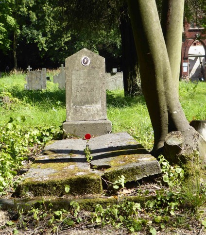 Nagrobek Jana Unuckiego z dwuspadową stelą na cokole, z owalnym medalionem fotograficznym i tablicą z inskrypcją. Grób otoczony zielenią i drzewami.