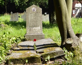 Nagrobek Jana Unuckiego z dwuspadową stelą na cokole, z owalnym medalionem fotograficznym i tablicą z inskrypcją. Grób otoczony zielenią i drzewami.