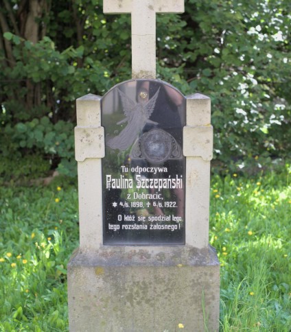 Nagrobek Pauliny Szczepańskiej z krzyżem na dwustopniowym cokole. Tablica inskrypcyjna z aniołem i tekstem po polsku, otoczona zielenią.